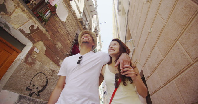  Happy couple on summer vacation walking through narrow city street, looking at the buildings. 