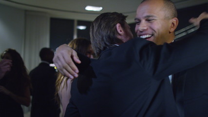  Cheerful male friends or business colleagues embrace at sophisticated party