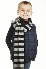 Funny child. fashionable little boy in  jeans, black shirt,  woolen  striped muffler and and padded vest .stylish  smiling  kid. fashion children