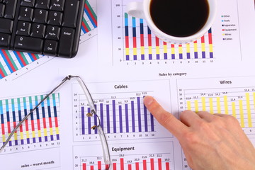 Finger showing financial graph, glasses, computer keyboard and cup of coffee, business concept
