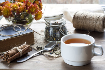 Cup of hot tea with books, tea leaves and flowers on wooden table. Vintage still life.