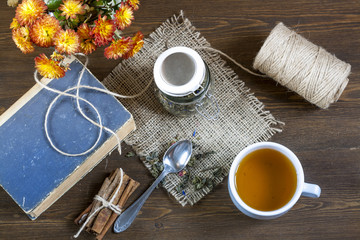 Cup of hot tea with books, tea leaves and flowers on wooden table. Vintage still life.