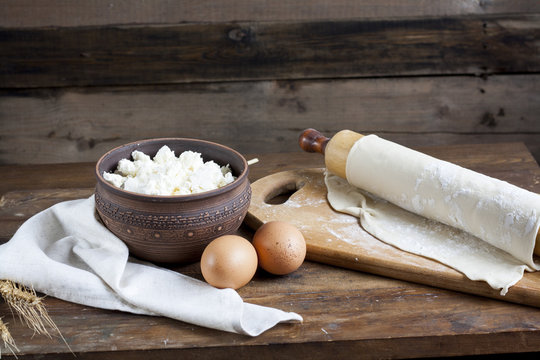 Rustic natural dairy products. Rustic natural dairy products cottage cheese in clay dishes, eggs ears and dough of wheat on the old wooden background.