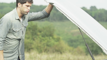 Stranded man with broken down car looks under the bonnet