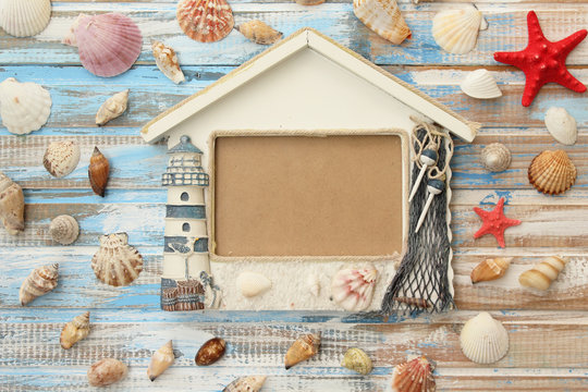 Summer sea decoration: lighthouse photo frame with star fish and shells on ocean color wooden background 