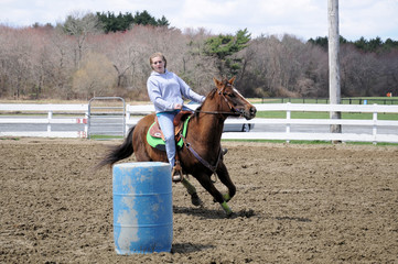 Pretty blonde teenage girl barrel racing; A young teenage girl turns around a barrel and races to the finish line