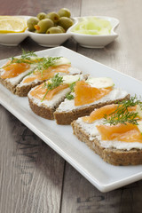 Sandwiches with salmon, ricotta, dill and cucumber on a wooden backgroundл On background platter with olives, cucumber and lemon.