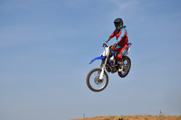 Motocross rider performs a jump on a motorcycle sideways looking at the camera, against a blue sky