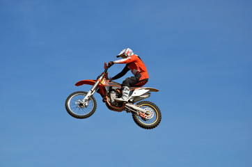 Freestyle tall flight on the MX bike athlete in the the form of an orange, on the background of the clear blue sky  