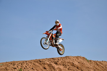 Fototapeta na wymiar MX rider on a motorbike jumps down the slope turning his head looking at the camera