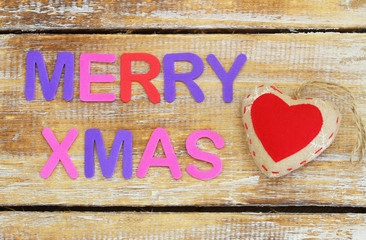 Merry Christmas written with colorful letters on wooden surface and red knitted heart
