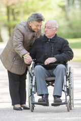 Wife holding hand of husband in wheelchair