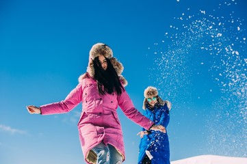 winter, two cheerful young girls having fun in the snow in the m