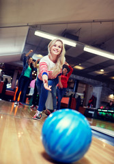 happy young woman throwing ball in bowling club