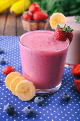 Glasses of fresh cold smoothie with fruit and berries, on blue tablecloth background