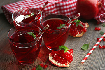 Three glasses of tasty juice and garnet fruit, on wooden background