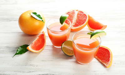 Two glasses of citrus juice and fresh fruits on light wooden background