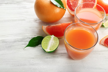 Two glasses of citrus juice and fresh fruits on light wooden background