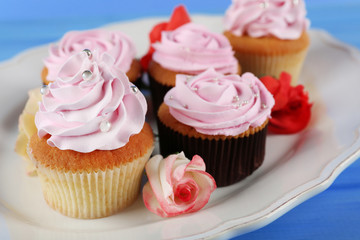 Tasty cupcakes on plate, on color wooden background