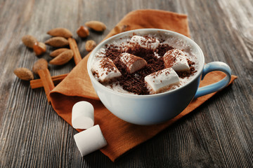 Cup of hot cacao with marshmallow, cinnamon and nuts on brown cotton serviette, close up
