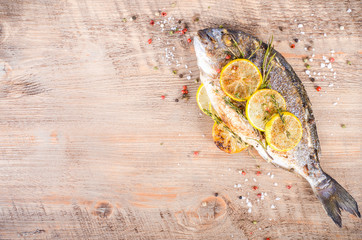 Roasted gilthead fishes with lemon, herbs, salt on wooden background. Healthy food concept. Food frame. Free space for your text.