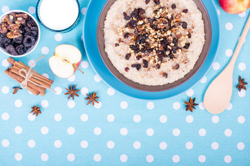 Breakfast set. A bowl of barley porridge with cocnut oil, vegetarian milk, walnuts, raisins, cinnamon on blue polka dot tablecloth, spoon, apple, glass of vegetarian milk. Free space for your text.