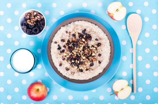 Breakfast set. A bowl of barley porridge with cocnut oil, vegetarian milk, walnuts, raisins, cinnamon on blue polka dot tablecloth, spoon, apple, glass of vegetarian milk. Free space for your text.