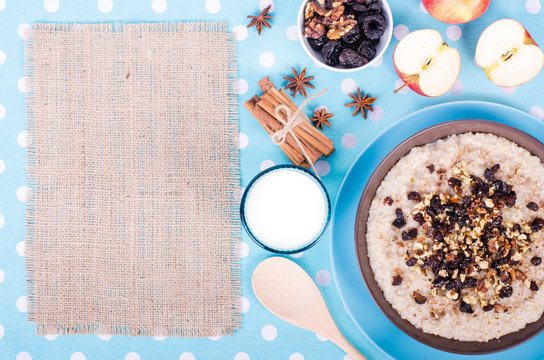 Breakfast set. A bowl of barley porridge with cocnut oil, vegetarian milk, walnuts, raisins, cinnamon on blue polka dot tablecloth, spoon, apple, glass of vegetarian milk. Free space for your text.