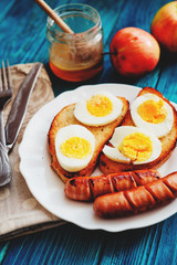 
breakfast or lunch , apples and honey , toasted croutons of white bread with boiled egg and fried sausages on a wooden background