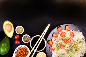 Chinese rice noodles with pesto, tomatoes cherry, avocado, soy sauce, lemon and spices on black background. Free space for your text.