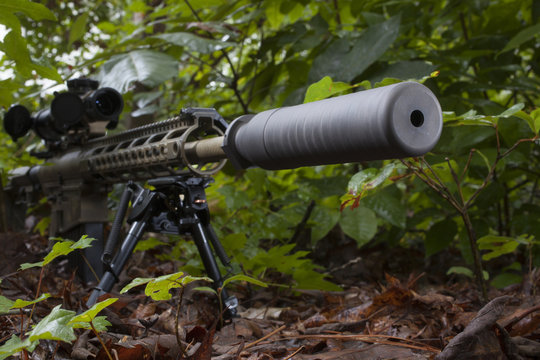 Silenced weapon resting on a bipod in a thick forest