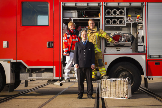 Portrait of happy firefighters and paramedic woman standing together before fire engine truck