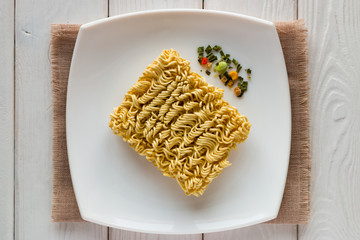 white plate with raw ramen noodles and dry vegetables