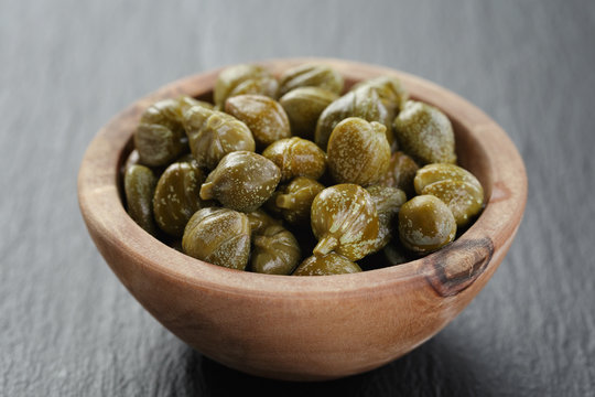 marinated capers in olive bowl on slate board