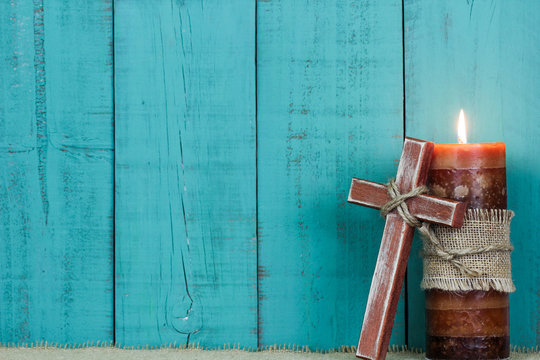 Candle and wooden cross by teal blue wood background