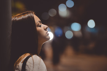 Sad young lady thinking about something leaning against street lamp