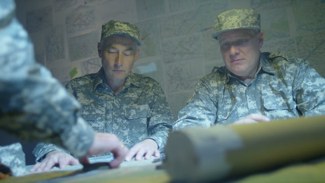  Military officers in army bunker, looking at map & discussing battle strategy