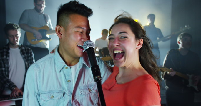 Young fun couple sing a duet with backing band at live music event