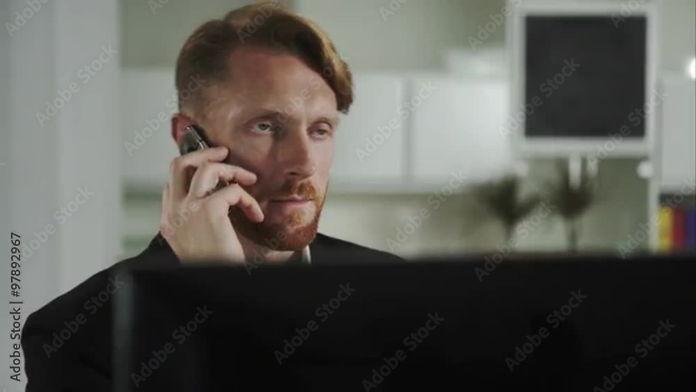 Poster Red-haired man sitting at a computer and calling on the phone