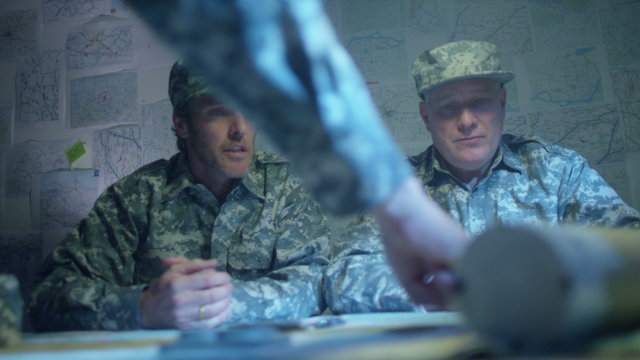  Military officers in army bunker, looking at map & discussing battle strategy
