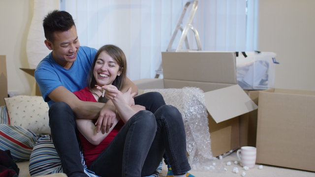  Happy young couple sitting amongst cardboard boxes with key to new home