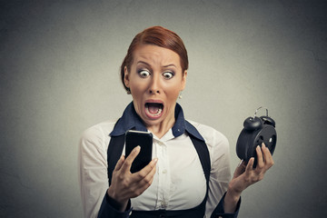 surprised business woman with alarm clock looking at smart phone