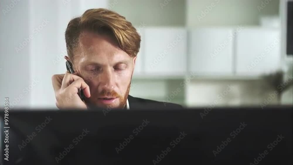 Poster Red-haired man sitting at a computer and calling on the phone
