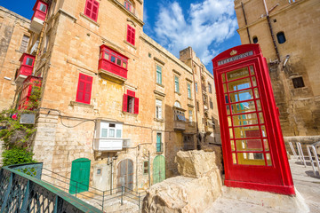 Old street of Valletta with red phone booth and traditional balconies and blue sky - Malta