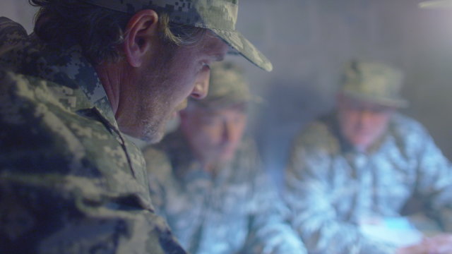  Military officers in army bunker, looking at map & discussing battle strategy