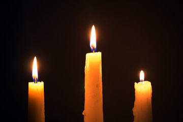 Three burning wax candles on a black background, religion, holid
