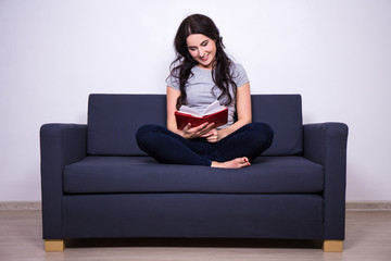Fototapeta na wymiar happy woman sitting on sofa and reading book