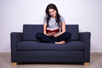 Obraz premium happy woman sitting on sofa and reading book