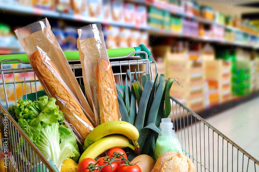 Wall mural shopping cart full of food in supermarket aisle elevated view