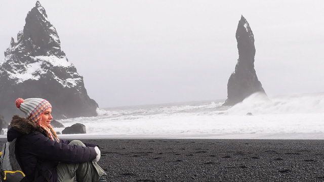 Cute young woman sitting on black beach of Iceland and enjoying beauty of Atlantic ocean, famous rocks of Vik Myrdal. Full HD Video 1920x1080